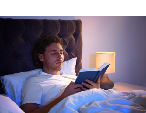 Afbeelding van een jonge man die in bed ligt en een boek aan het lezen is